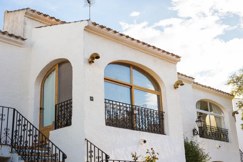 White stucco home with arched windows and wrought-iron balconies against a clear sky