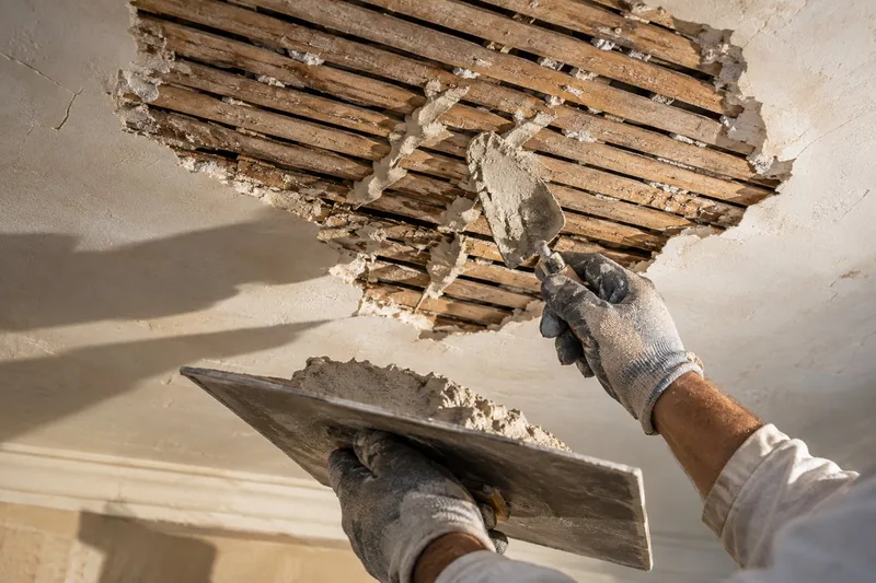 Fresh plaster pressed through the gaps in old wood lath to form new keys on an opened ceiling